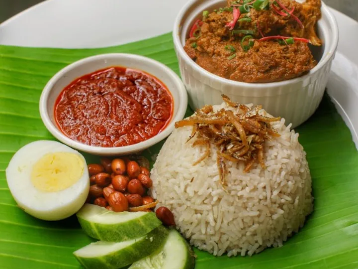 Nasi Lemak Aunty Aini di atas daun pisang bersama sambal, ikan bilis, kacang tanah, telur rebus dan hirisan timun